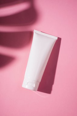 Krem veya losyon için plastik beyaz tüp. Cilt bakımı ya da güneş kremi pembe arka planda, palmiye yapraklarının gölgesinde. Yüz bakımı için güzellik konsepti