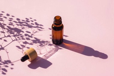 Şişeyi damlalık pipetle serumla ya da gerekli yağla açın. Pembe arka plan ve gün ışığı. Cilt bakım ürünleri, doğal kozmetik ürünleri. Yüz ve vücut bakımı için güzellik konsepti
