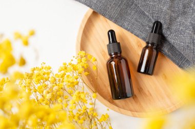 Ahşap tabakta siyah kapaklı Amber cam damlaları sunum için. Sarı kuru bitkiler ve kumaşlı gri kumaşa cilt bakımı kozmetiği. Yüz bakımı için güzellik konsepti