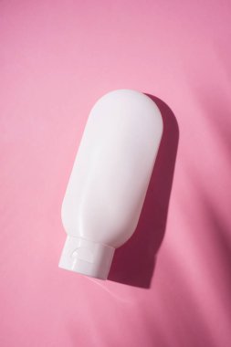 Krem veya losyon için plastik beyaz tüp. Cilt bakımı ya da güneş kremi pembe arka planda, palmiye yapraklarının gölgesinde. Yüz bakımı için güzellik konsepti