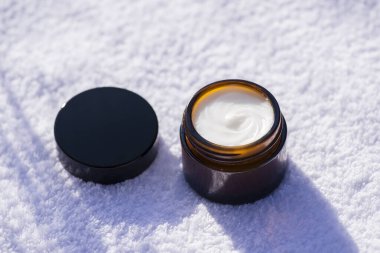 Kehribar rengi cam kavanozu beyaz havlunun arka planına krema desenli aç. Cilt bakım ürünleri, doğal kozmetik ürünleri. Yüz bakımı için güzellik konsepti