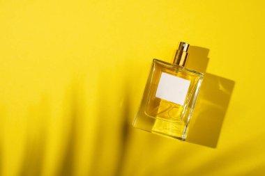 Sarı arka planda etiketi olan saydam bir parfüm şişesi. Gün ışığıyla güzel kokulu bir sunum. Doğal malzemelerdeki güzel gölgeli moda konsept. Kadın özü..