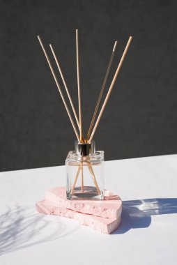 Açık gri arka planda şeffaf bir aroma yayıcı şişesi. Eau de parfum, bitki gölgeli bir podyumda sunum için. Doğal malzemelerde trend kavramı.