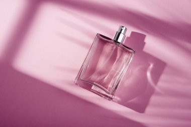 Pembe arka planda saydam bir parfüm şişesi. Gün ışığıyla güzel kokulu bir sunum. Pencere gölgesi olan doğal malzemelerde moda bir kavram. Kadın özü..