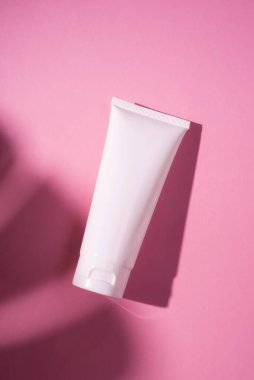 Krem veya losyon için plastik beyaz tüp. Cilt bakımı ya da güneş kremi pembe arka planda, palmiye yapraklarının gölgesinde. Yüz bakımı için güzellik konsepti