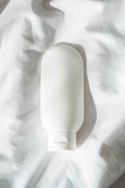 Krem için plastik beyaz tüp ya da hafif kumaş arka planında losyon. Güneş ışığı ve güzel gölgeli cilt bakım kozmetik sunumu. Yüz bakımı için güzellik konsepti.