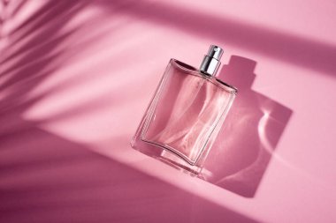 Pembe arka planda saydam bir parfüm şişesi. Gün ışığıyla güzel kokulu bir sunum. Pencere gölgesi olan doğal malzemelerde moda bir kavram. Kadın özü..