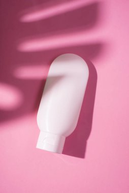 Krem veya losyon için plastik beyaz tüp. Cilt bakımı ya da güneş kremi pembe arka planda, palmiye yapraklarının gölgesinde. Yüz bakımı için güzellik konsepti