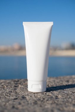 Plastik beyaz tüp, deniz ve plajın bulanık arka planında krem ya da losyon için. Güzel gölgeli cilt bakımı kozmetiği. Yüz bakımı için güzellik konsepti.