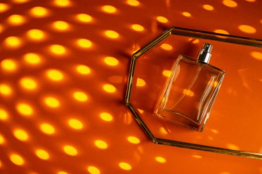 Turuncu arka planda cam tepside saydam bir parfüm şişesi. Gün ışığıyla güzel kokulu bir sunum. Doğal malzemelerdeki güzel gölgeli moda konsept. Kadın özü..