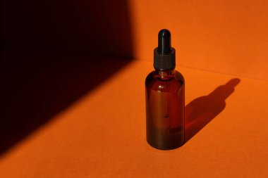 Damla pipetli bir şişe serum ya da gerekli yağ. Turuncu arka plan ve gün ışığı. Cilt bakım ürünleri, doğal kozmetik ürünleri. Yüz ve vücut bakımı için güzellik konsepti
