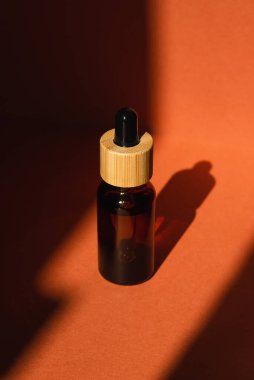 Damla pipetli bir şişe serum ya da gerekli yağ. Turuncu arka plan ve gün ışığı. Cilt bakım ürünleri, doğal kozmetik ürünleri. Yüz ve vücut bakımı için güzellik konsepti