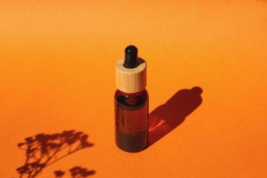 Damla pipetli bir şişe serum ya da gerekli yağ. Turuncu arka plan, gün ışığı ve güzel bitki gölgeleri. Cilt bakım ürünleri, doğal kozmetik ürünleri. Yüz ve vücut bakımı için güzellik konsepti