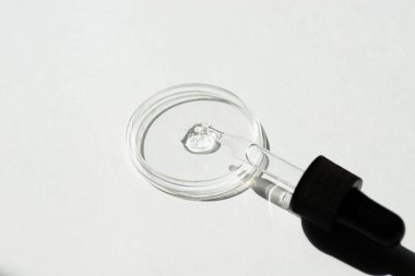 Beyaz zemin üzerinde serum ya da kozmetik sıvısı ve petri kabı olan damlatan pipet. İçi sıvı ve kabarcıklarla dolu şeffaf bir kap. Jel dokusunun görünüşü. Tıp ve güzellik konsepti.