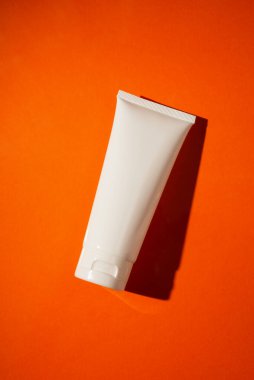 Krem veya losyon için plastik beyaz tüp. Turuncu arka planda güzel gölgeli cilt bakımı ya da güneş kremi. Yüz bakımı için güzellik konsepti