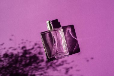 Mor arka planda şeffaf bir parfüm şişesi. Gün ışığıyla güzel kokulu bir sunum. Doğal malzemelerde bitki gölgesiyle moda olan kavram. Kadın ve erkeğin özü..