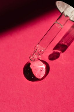 Kapağı serumla birlikte yakın çekim damlatıcısıyla aç. Pipete odaklan. Kırmızı arka plan, gün ışığı ve jel dokusunun görünüşü. Cilt bakım ürünleri, doğal kozmetik ürünleri.