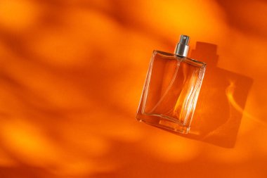 Turuncu arka planda saydam bir parfüm şişesi. Gün ışığıyla güzel kokulu bir sunum. Güzel gölgeli trend konsepti. Kadın özü..