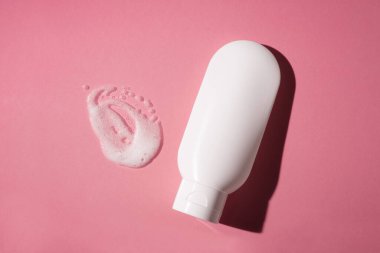 Plastik beyaz tüp ve pembe arka plandaki köpük dokusunun görünüşü. Cilt bakımı ya da güzel gölgeli pembe arka planda güneş kremi. Yüz bakımı için güzellik konsepti