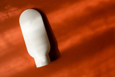Krem veya losyon için plastik beyaz tüp. Cilt bakımı ya da güneş kremi turuncu arka planda güzel gölgeli üst görünümde. Yüz bakımı için güzellik konsepti