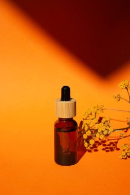 Damla pipetli bir şişe serum ya da gerekli yağ. Turuncu arka plan, gün ışığı ve güzel bitki gölgeleri. Cilt bakım ürünleri, doğal kozmetik ürünleri. Yüz ve vücut bakımı için güzellik konsepti