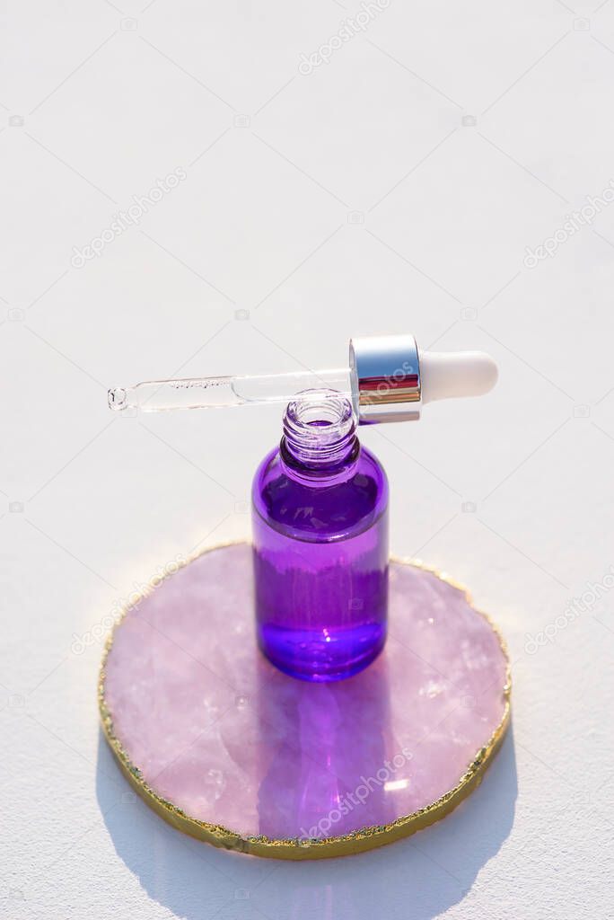 Open purple glass bottle with dropper pipette with serum or essential oil. White background with daylight. Skincare products , natural cosmetic. Beauty concept for face and body care