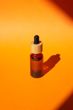 Damla pipetli bir şişe serum ya da gerekli yağ. Turuncu arka plan, gün ışığı ve güzel gölgeler. Cilt bakım ürünleri, doğal kozmetik ürünleri. Yüz ve vücut bakımı için güzellik konsepti