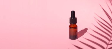 Damla pipetli bir şişe serum ya da gerekli yağ. Pembe arka plan, gün ışığı ve güzel palmiye gölgeleri. Kincare ürünleri, doğal kozmetik. Yüz ve vücut bakımı için güzellik konsepti