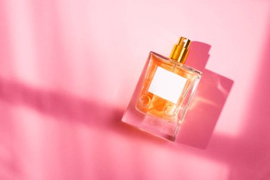 Pembe arka planda etiketi olan saydam bir parfüm şişesi. Gün ışığıyla güzel kokulu bir sunum. Doğal malzemelerdeki güzel gölgeli moda konsept. Kadın ve erkeğin özü..