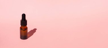 Damla pipetli bir şişe serum ya da gerekli yağ. Pembe arka plan, gün ışığı ve güzel gölge. Cilt bakım ürünleri, doğal kozmetik ürünleri. Yüz ve vücut bakımı için güzellik konsepti