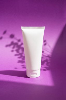 Krem veya losyon için plastik beyaz tüp. Cilt bakımı ya da güneş kremi güzel gölgeli mor arka planda üst görünümde. Yüz bakımı için güzellik konsepti