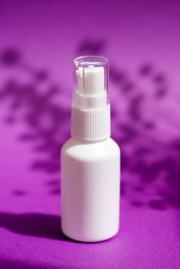 Krema için pompalı plastik beyaz şişe ya da mor arka planda bitkilerin gölgesi olan losyon. Cilt bakımı. Yüz bakımı için güzel bir konsept.