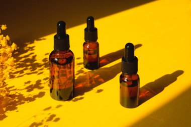 Kehribar şişelerinde damla pipeti ve serum ya da gerekli yağ var. Sarı arka plan, gün ışığı, güzel çiçekler ve gölgeler. Cilt doğal kozmetik. Yüz ve vücut bakımı için güzellik konsepti