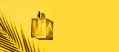 Sarı arka planda etiketi olan saydam bir parfüm şişesi. Gün ışığıyla güzel kokulu bir sunum. Doğal malzemelerdeki güzel gölgeli moda konsept. Kadın özü..