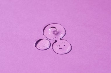 Şeffaf kozmetik ürün serumu jeli damlası. Üst görünümde mor arkaplanda kabarcıklar olan sıvı doku. Cilt bakım ürünleri, doğal kozmetik ürünleri. Yüz ve vücut bakımı için güzellik konsepti