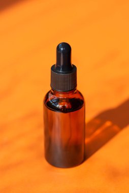 Kehribar şişesinde damla pipeti ve serum ya da gerekli yağ. Turuncu arka plan, gün ışığı ve güzel gölgeler. Cilt bakım ürünleri, doğal kozmetik ürünleri. Yüz ve vücut bakımı için güzellik konsepti