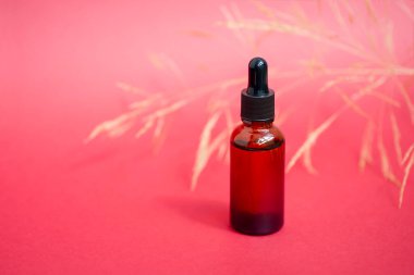 Damla pipetli bir şişe serum ya da gerekli yağ. Kırmızı arka plan, gün ışığı ve sarı çiçekler. Cilt bakım ürünleri, doğal kozmetik ürünleri. Yüz ve vücut bakımı için güzellik konsepti