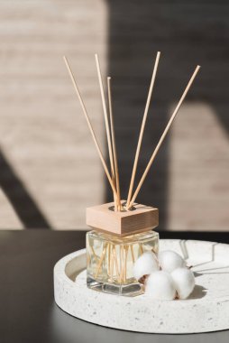 Bulanık oda arka planında terazzo podyumunda şeffaf bir şişe aroma yayıcı var. Podyumda pamuk çiçeklerle sunum için parfüm. Doğal malzemelerde trend kavramı.