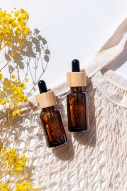 Kehribar şişesi ve damlatan pipetle serum ya da kumaş alışveriş torbası ve güzel çim. Beyaz arka plan, gün ışığı ve gölgeler. Yüz ve vücut bakımı için güzellik konsepti