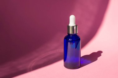 Damla pipetli mavi şişe, serum ya da gerekli yağ. Pembe arka plan, gün ışığı ve güzel gölgeler. Cilt bakım ürünleri, doğal kozmetik ürünleri. Yüz ve vücut bakımı için güzellik konsepti