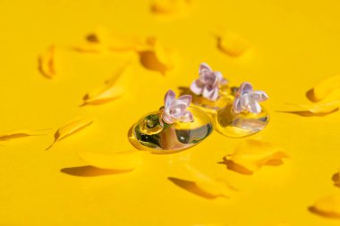 Şeffaf kozmetik ürün serumu ya da leylak çiçekli ve sarı yapraklı jel damlaları. Baloncuklu sıvı doku. Kozmetik lekesi. Yüz ve vücut bakımı için güzellik konsepti