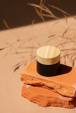 Siyah kozmetik kavanozu, kremalı ahşap kapak ya da kaya kaidesi üzerinde lotyon. Ürün sunumu için kırmızı beton podyumda bir şişe. Cilt bakım ürünleri ve kır çiçekleri. Yüz ve vücut bakımı için güzellik konsepti