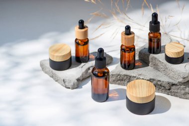 Bambu kapaklı ve siyah kavanozlu kehribar cam damlası. Ürün sunumu için gri beton podyumda bir şişe. Cilt bakım ürünleri ve kır çiçekleri. Güzellik konsepti