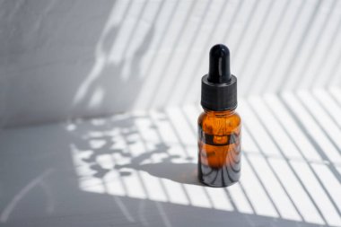 Damla pipetli bir şişe serum ya da gerekli yağ. Beyaz arka plan, gün ışığı ve güzel köşegen gölgeler. Cilt bakım ürünleri, doğal kozmetik ürünleri. Yüz ve vücut bakımı için güzellik konsepti