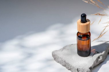 Bambu kapaklı ve kuru bitkili kehribar cam damlası. Ürün sunumu için gri beton podyumda bir şişe. Cilt bakım ürünleri ve kır çiçekleri. Güzellik konsepti