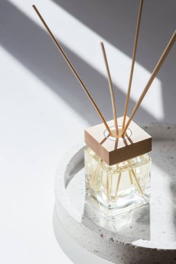 Beyaz arka planda terrazzo podyumunda şeffaf bir şişe aroma yayıcı var. Ev yapımı sunum için parfüm. Moda konsepti. Sarı sıvı ve ahşap kaplama