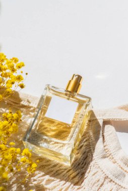 Beyaz arka planda etiketi ve kumaş alışveriş çantası olan şeffaf bir parfüm şişesi. Gün ışığıyla güzel kokulu bir sunum. Doğal malzemelerde sarı tarla çiçekleriyle moda olan bir kavram. Kadın ve erkeğin özü..