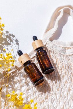 Kehribar şişe damlası pipeti, serum ya da gerekli yağ ve bez torbası, güzel bir tarla çimeni. Beyaz arka plan, gün ışığı ve gölgeler. Yüz bakımı için güzellik konsepti