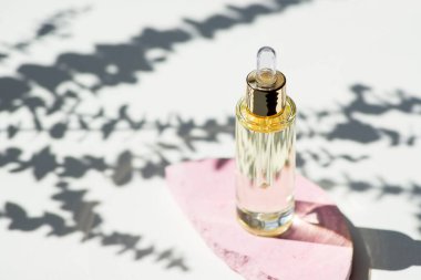 Damlatan pipetli şeffaf bir şişe serum ya da okaliptüs gölgeli pembe beton podyumda gerekli yağ. Gündüz vakti beyaz arka plan. Yüz ve vücut bakımı için güzellik konsepti