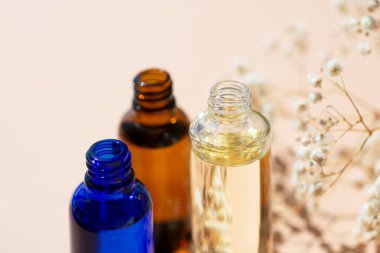 Kehribar, mavi ve şeffaf şişeler serumla kaplanmamış ya da beyaz çiçeklerle yağlanmamış. Bej arka plan, gün ışığı ve güzel gölgeler. Yüz ve vücut bakımı için güzellik konsepti